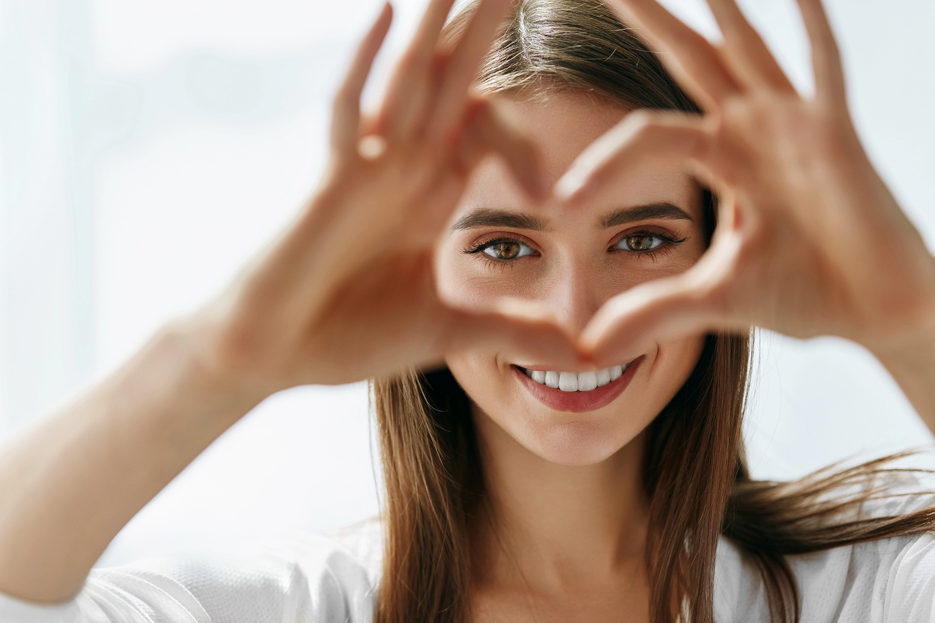Young woman is forming her hands like a heart in from of her eyes after light adjustable lens correction